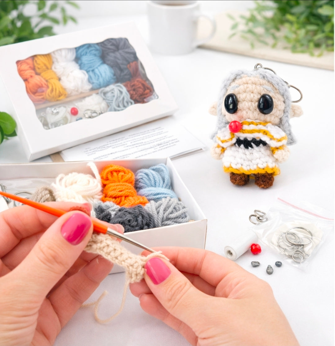 Complete Friren crochet kit showing a crocheter holding yarn & crochet hook, stuffing, handmade accessories, and printed crochet pattern booklet