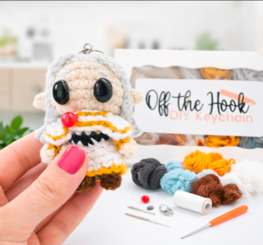 Complete Friren crochet kit showing yarn, crochet hook, stuffing, handmade accessories, and the finished keychain in hand