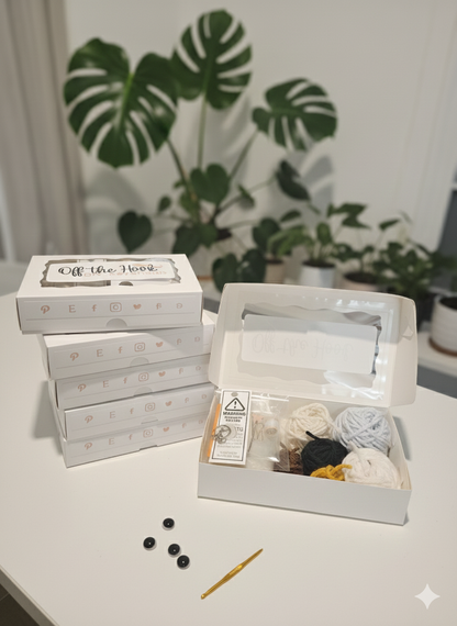 Image of the open kit next to a pile of other kits on a white desk with a monstera plant in background. 